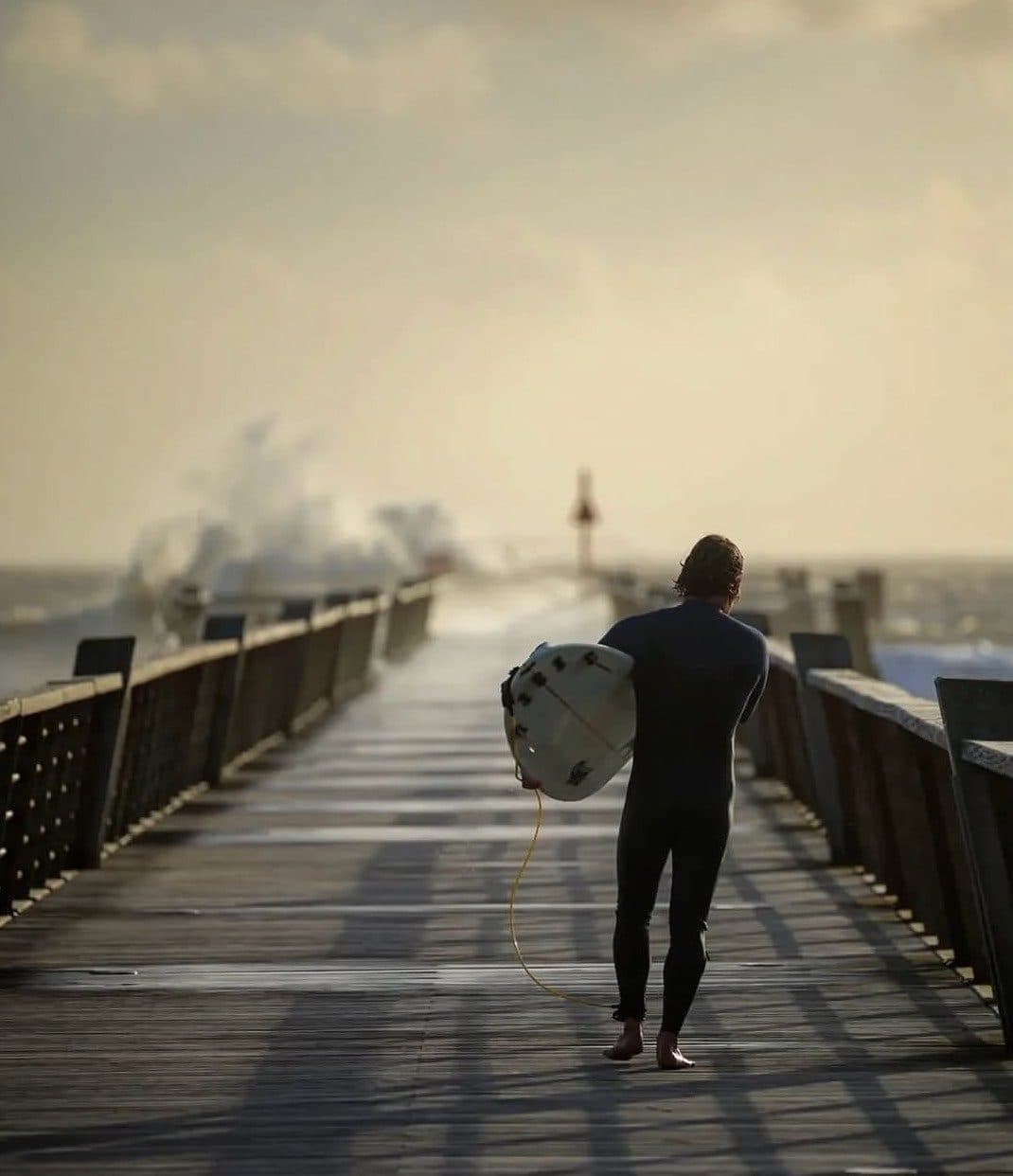 Un surfeur remonte l’estacade dans la brume du matin