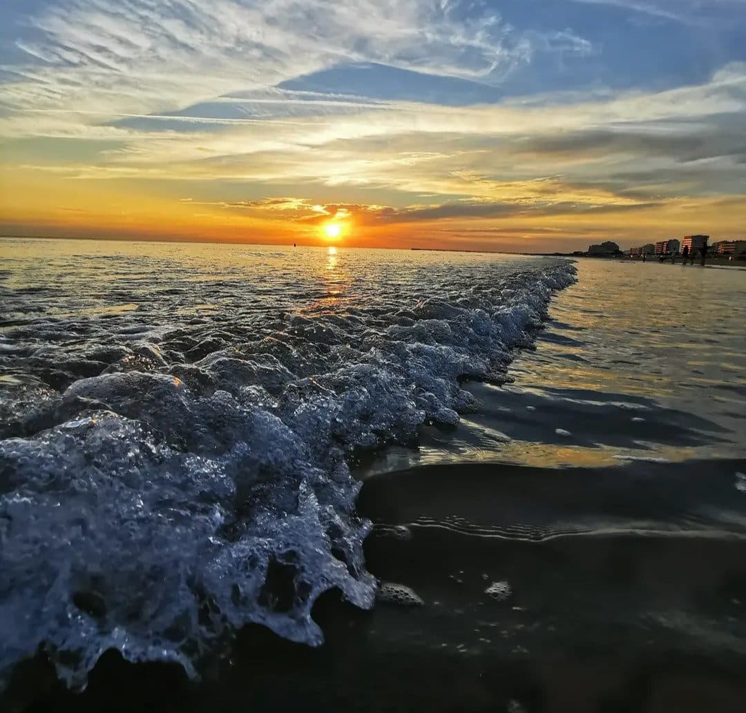 Le soleil couchant derrière une vague qui s’étale sur le sable