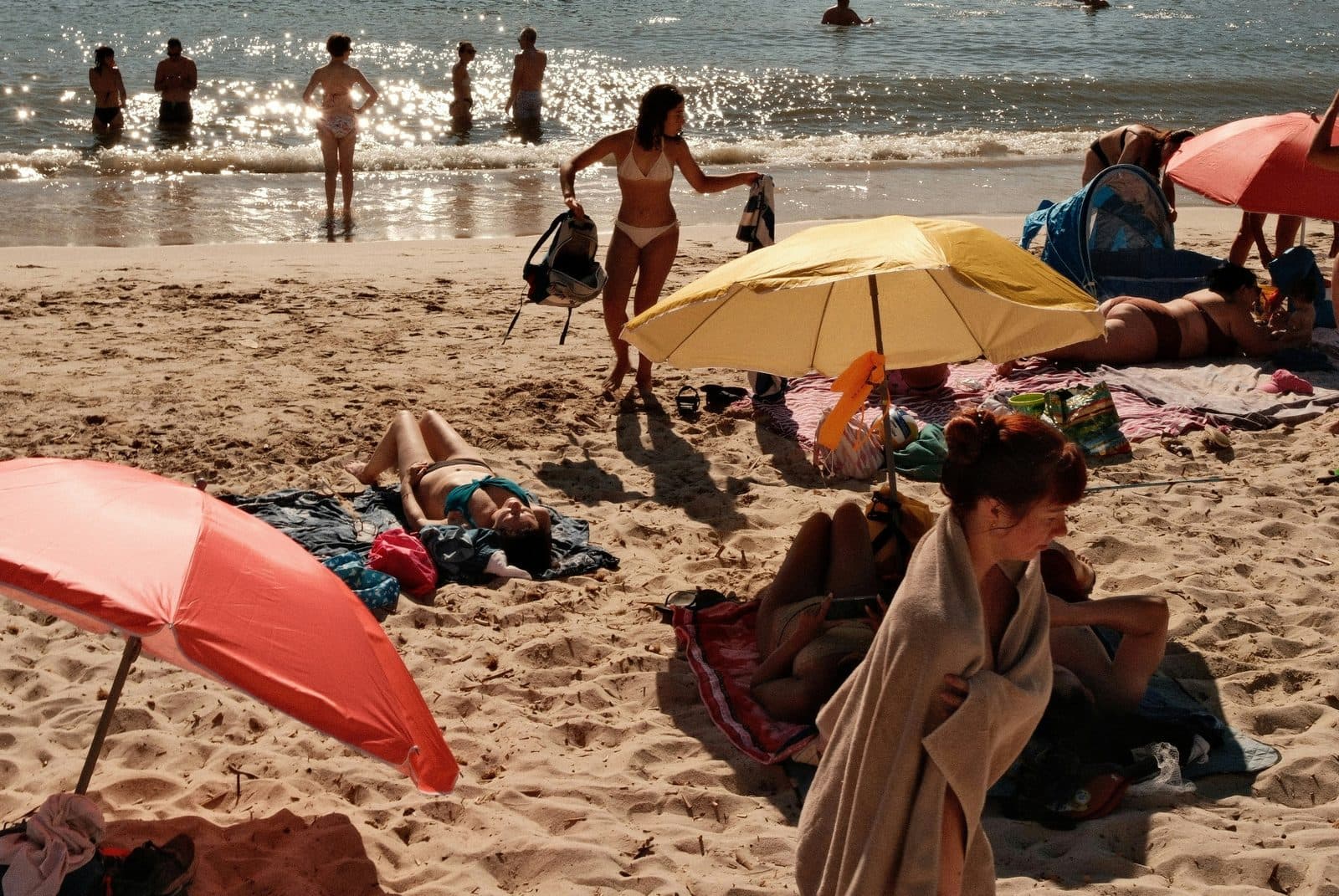 Une plage animée l’après-midi : parasols, serviettes et baigneurs au bord de l’eau