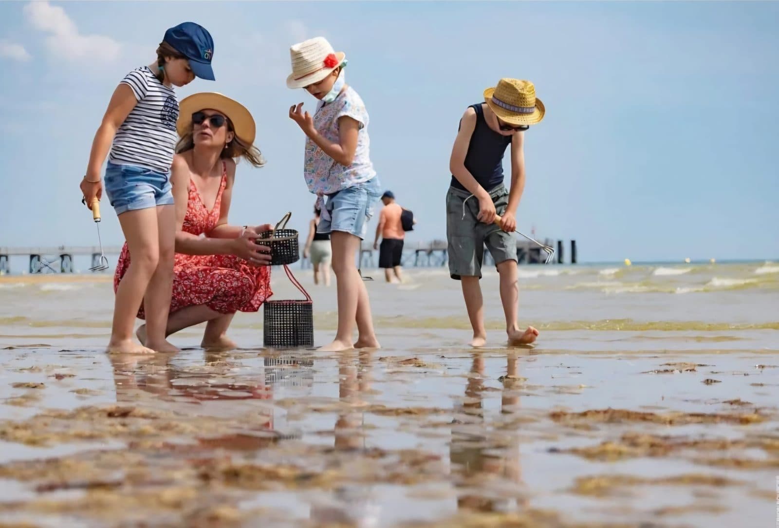 Une mère et ses trois enfants penchés sur un seau, sur le sable mouillé