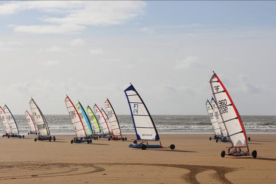 Une flotte de chars à voile colorés alignés sur le sable